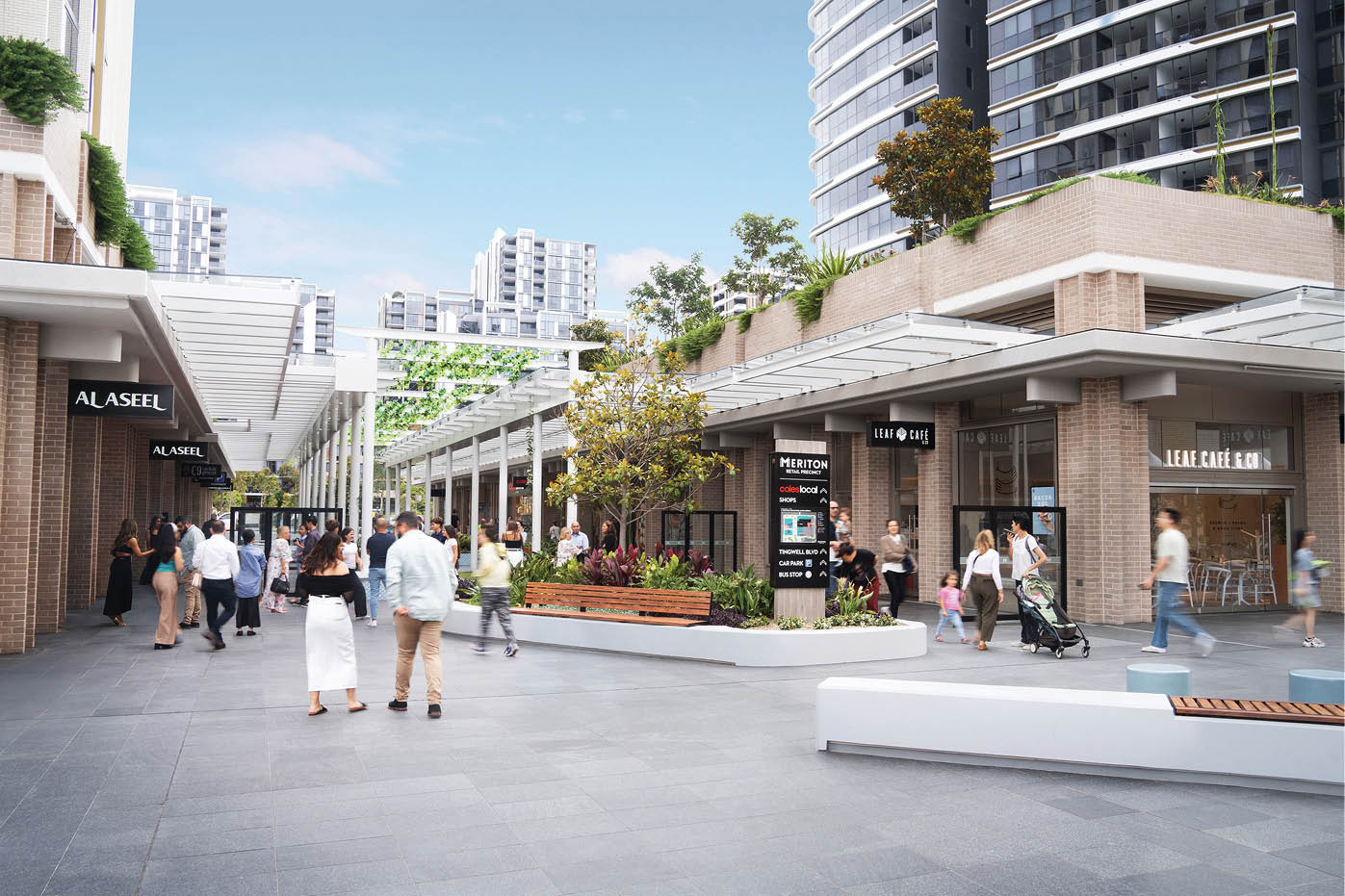 A modern outdoor shopping area with people walking, some pushing strollers, surrounded by tall buildings, greenery, and retail stores. Description generated by AI