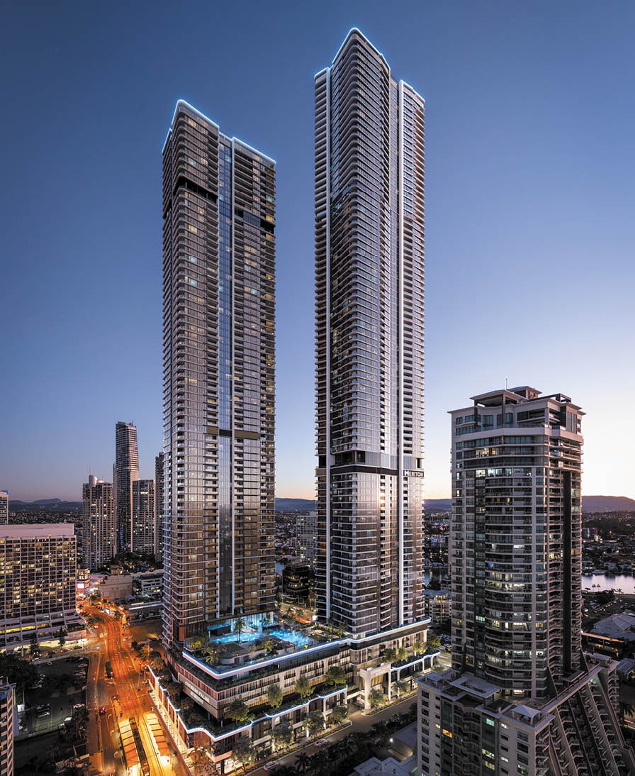 Two tall modern skyscrapers with illuminated balconies stand prominently in a cityscape at dusk with surrounding buildings and streets lit by streetlights. Description generated by AI