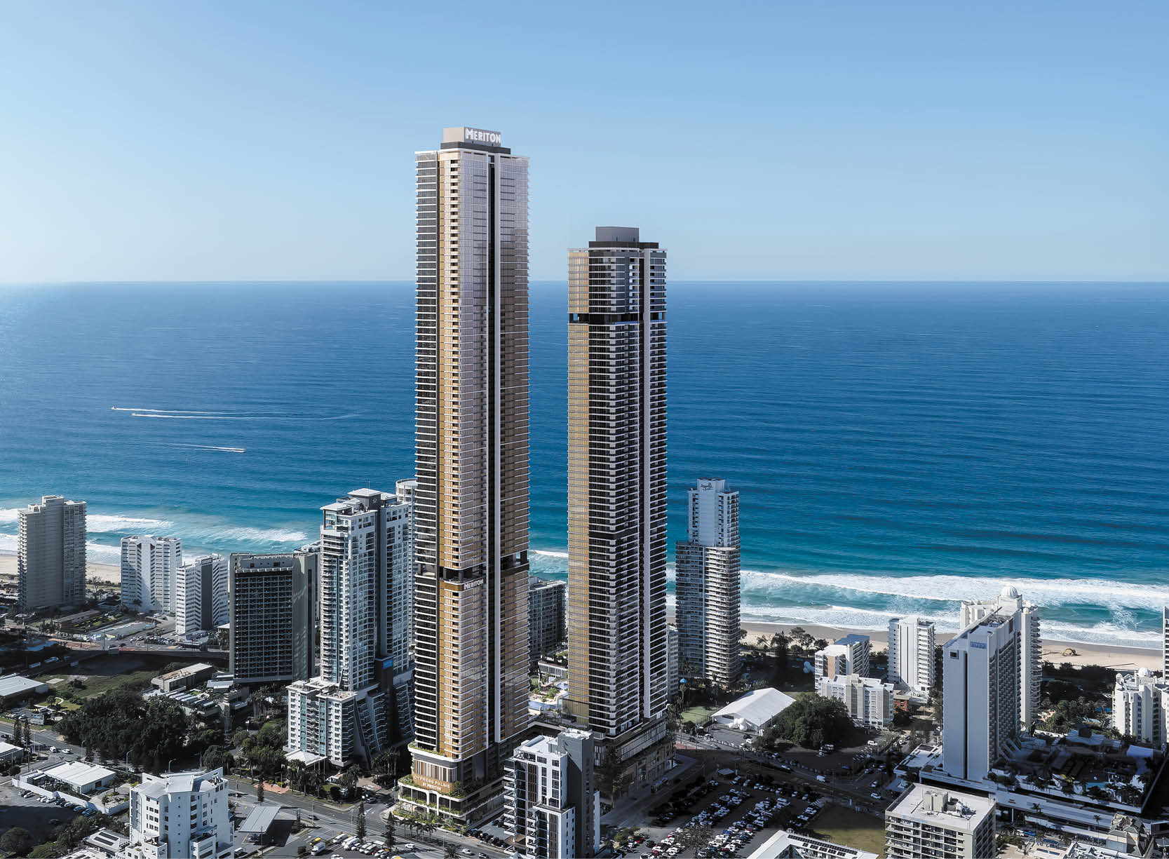 Two tall modern skyscrapers stand prominently near a coastline with smaller buildings surrounding them and the ocean stretching out in the background under a clear blue sky. Description generated by AI