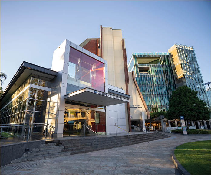 A modern building complex with glass facades and a paved walkway in front under a clear blue sky. Description generated by AI