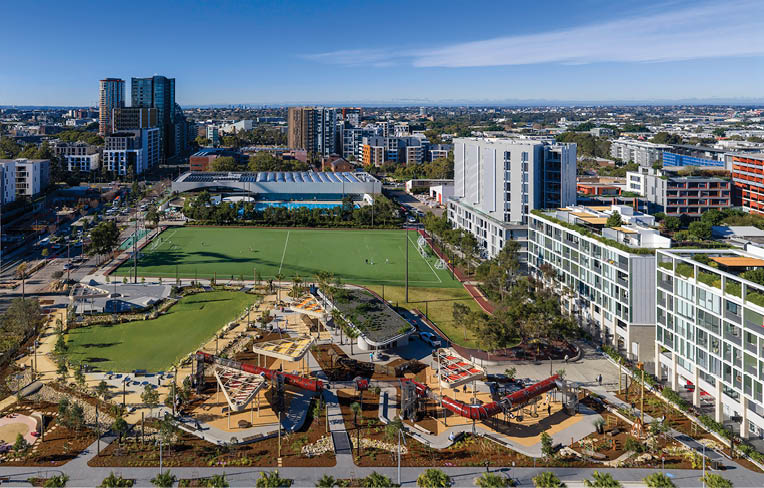 An outdoor swimming pool with lanes is surrounded by a modern building, lounge chairs with umbrellas, and greenery in an urban setting. Description generated by AI