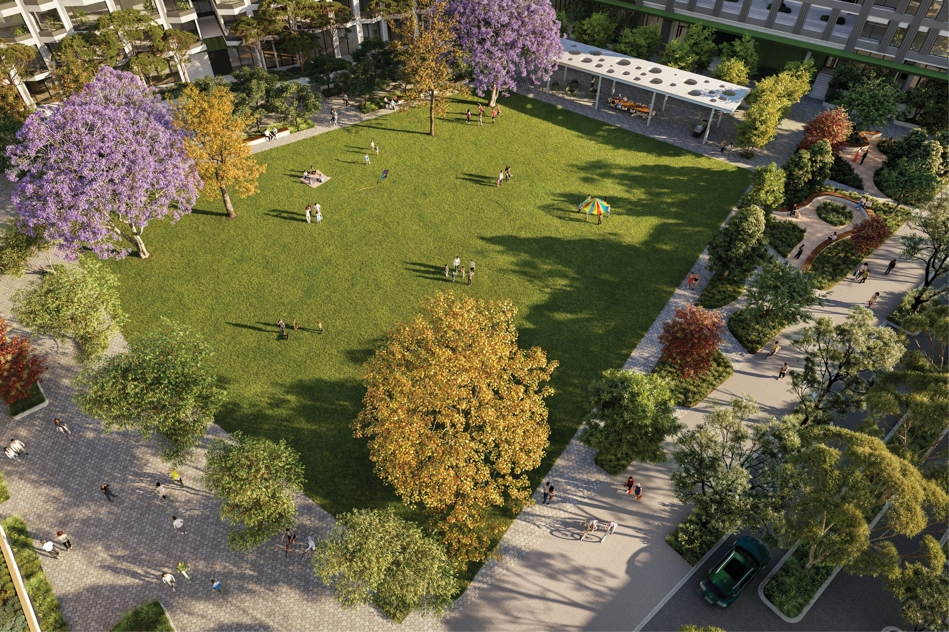A sunlit urban park with green grass, colorful trees, people walking and sitting, and a nearby building with outdoor seating. Description generated by AI